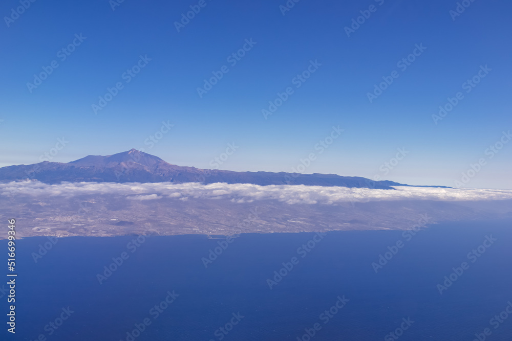 Window view from an airplane on the volcano mountain peak of Pico del Teide on Tenerife, Canary Islands, Spain, Europe, EU. High peak are shrouded in clouds. Flying high above the ground. Freedom