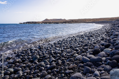 Panoramic view on black stone pebble beach Playa Colmenares near Amarilla, Golf del Sur, Tenerife, Canary Islands, Spain, Europe. Montana Amarilla in the back. Tranquil waves from the Atlantic Ocean © Chris