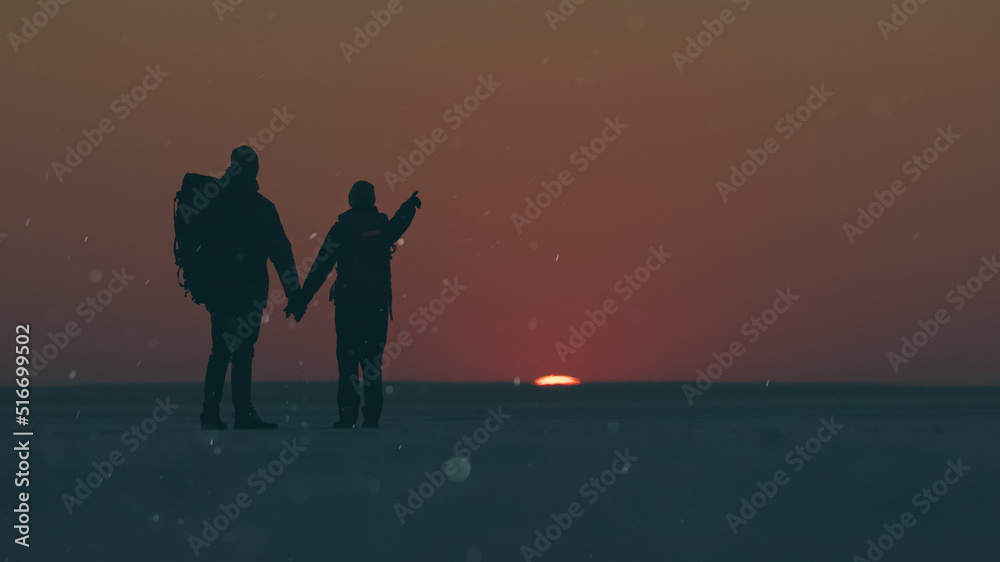 Fototapeta premium The two travelers standing through the snow field against beautiful sunset