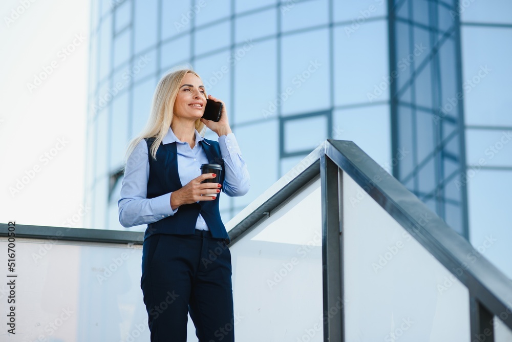 Business Woman With Phone Near Office. Portrait Of Beautiful Smiling Female In Fashion Office Clothes Talking On Phone While Standing Outdoors. Phone Communication. High Quality Image. Business Woman With Phone Near Office. Portrait Of Beautiful Smiling Female In Fashion Office Clothes Talking On Phone While Standing Outdoors. Phone Communication. High Quality Image.