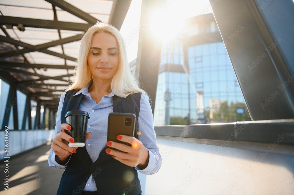 Fototapeta premium Business Woman With Phone Near Office. Portrait Of Beautiful Smiling Female In Fashion Office Clothes Talking On Phone While Standing Outdoors. Phone Communication. High Quality Image.