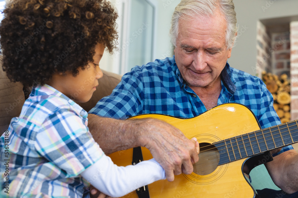 Caucasian senior man teaching playing guitar to biracial grandson while sitting at home Caucasian senior man teaching playing guitar to biracial grandson while sitting at home