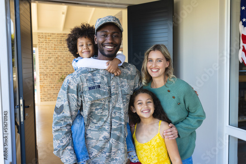 Portrait of happy multiracial soldier with woman and children standing at entrance of house photo