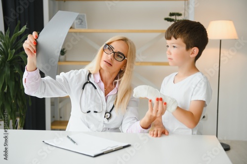 Female senior pediatrician showing x-ray of wrist and hand to little boy patient. Child at doctors office photo