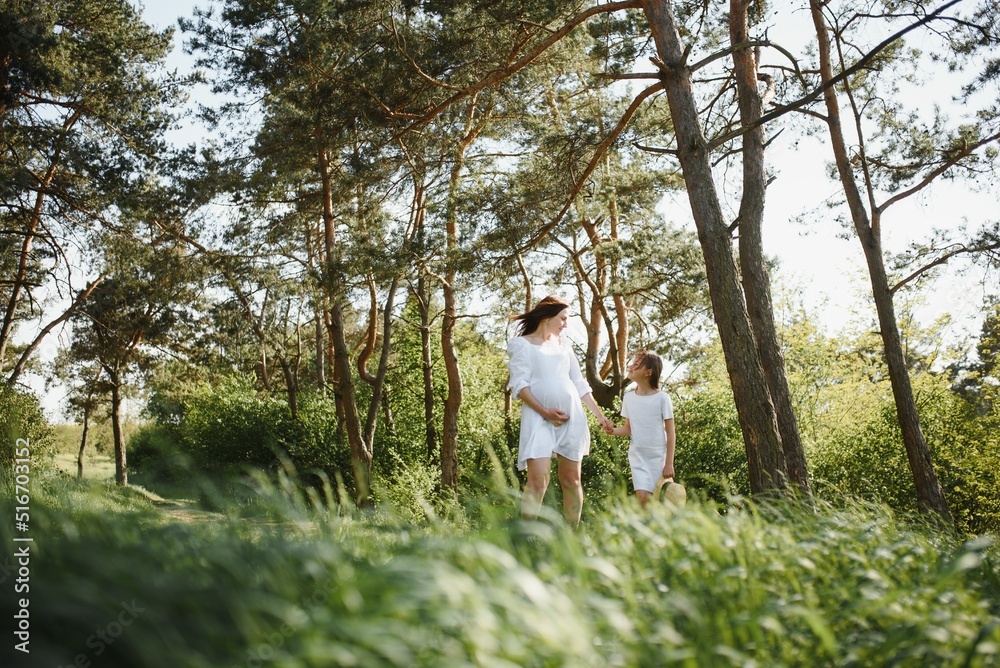 Pregnant woman and her daughter in the park at sunset. A happy family. Pregnant woman and her daughter in the park at sunset. A happy family.