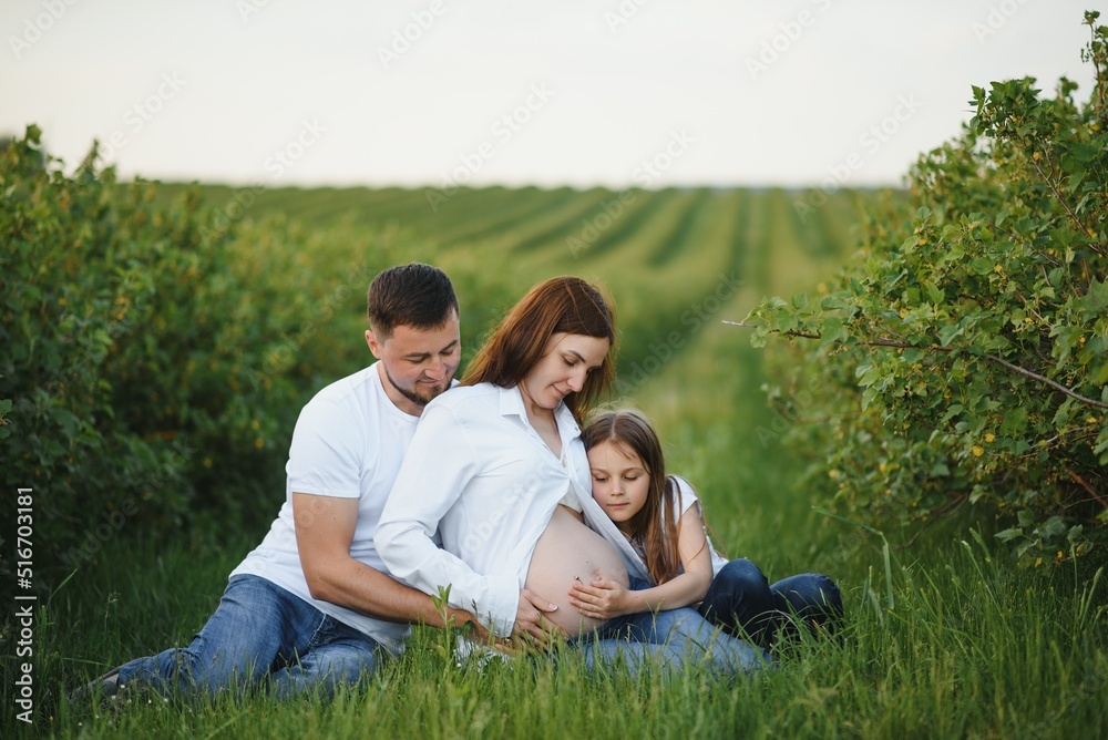 Beautiful pregnant brunette mom and dad and dauther in white clothes look at each other in nature. Beautiful pregnant brunette mom and dad and dauther in white clothes look at each other in nature.