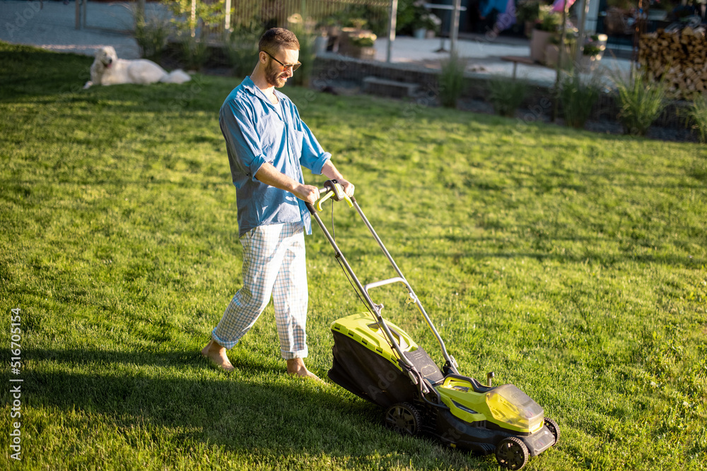 Man mows the lawn with lawn mower at backyard of his house. Husband