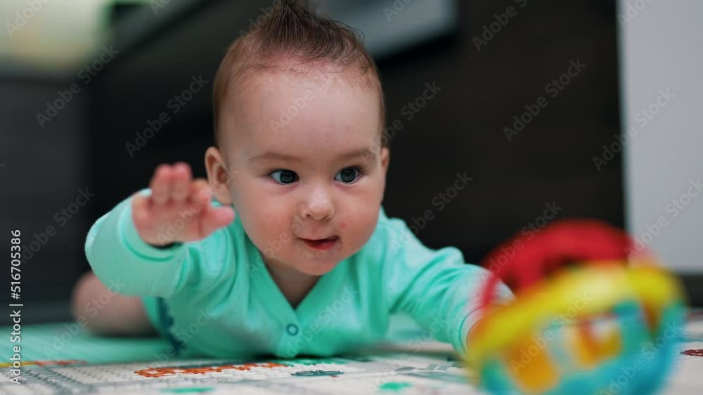 Adorable infant baby with funny hairdo claps his hands by the floor. Child looks curiously at toy showing tongue. Adorable infant baby with funny hairdo claps his hands by the floor. Child looks curiously at toy showing tongue.