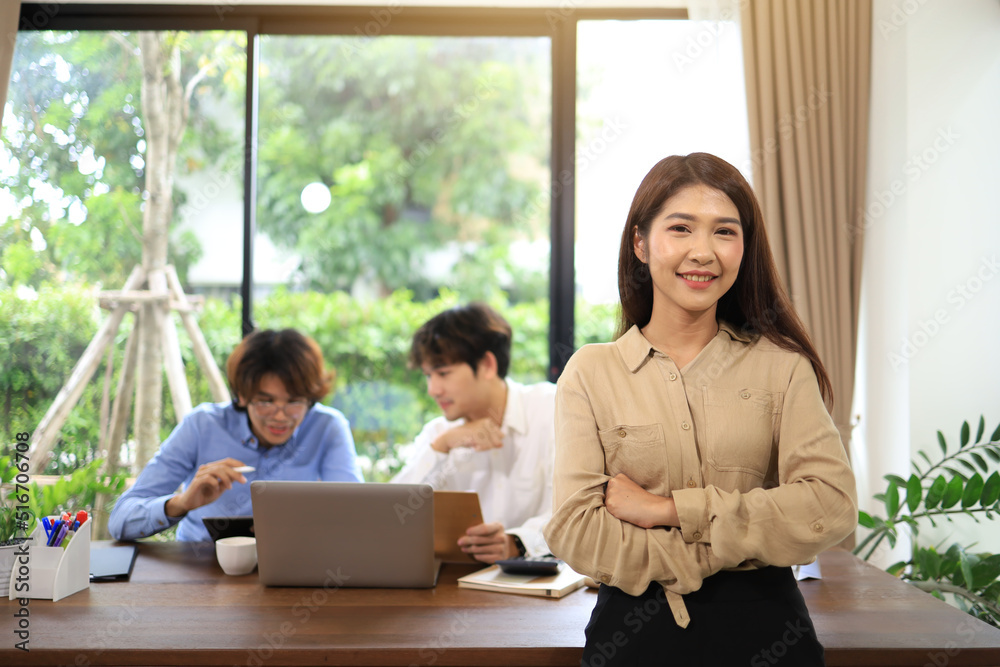 A businesswoman with her arms crossed to show her success as a leader and smart background is a subordinate working at the desk.