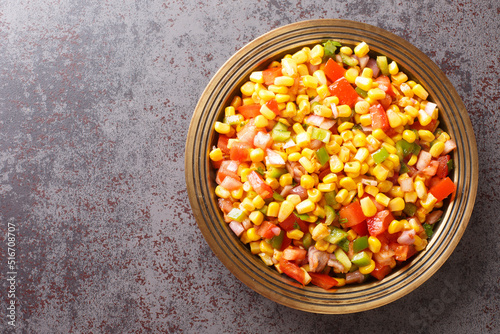 Corn chaat is a super quick snack made with boiled corn, chaat masala, spice powder, onions and tomatoes on a plate closeup on the table. Horizontal top view from above