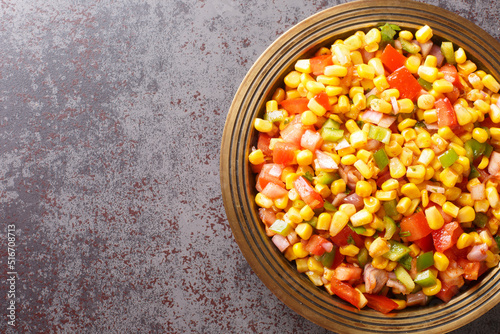 Sweet Corn Chaat is a tangy, spiced and tasty snack made with steamed or boiled sweet corn, onions, tomatoes, herbs and spices on a plate closeup on the table. Horizontal top view from above