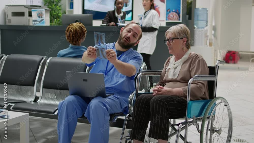 Patient with chronic disability looking at x ray scan results to talk about physical diagnosis and impairment with medical assistant in waiting room. Wheelchair user receiving bones radiography. Patient with chronic disability looking at x ray scan results to talk about physical diagnosis and impairment with medical assistant in waiting room. Wheelchair user receiving bones radiography.