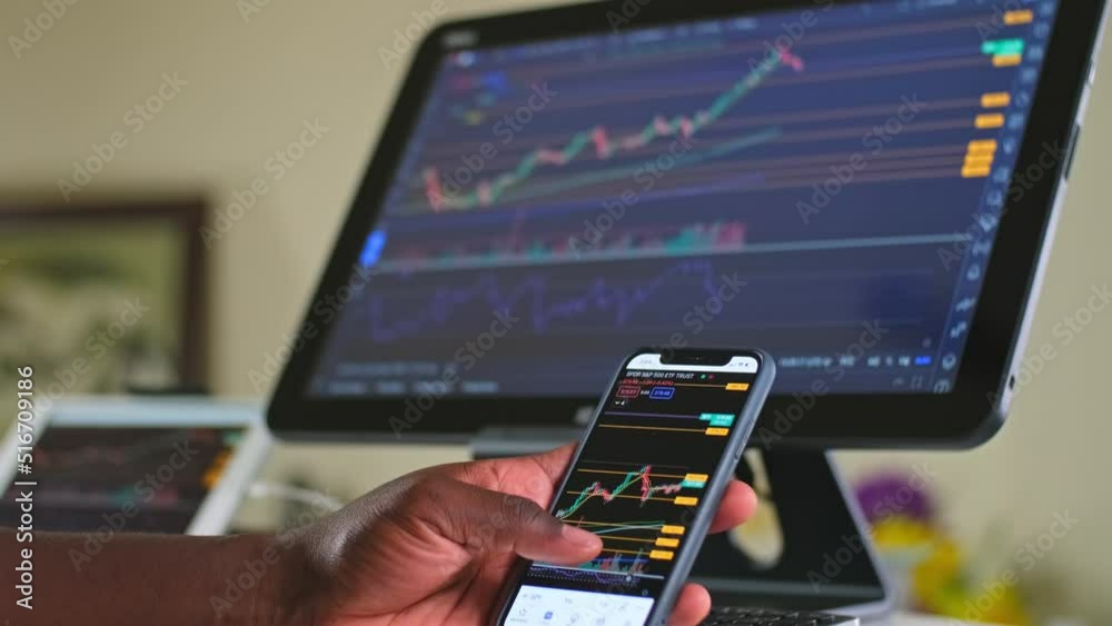 Man swiping with his thumb stock charts while day trading on his cellphone and his computer at his home office area working from home. Man swiping with his thumb stock charts while day trading on his cellphone and his computer at his home office area working from home.