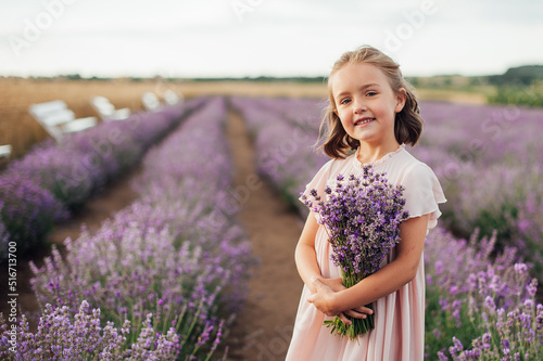 pretty little girl wearing pink dress with a bouquet in hands is standing among lavender field, horizontal