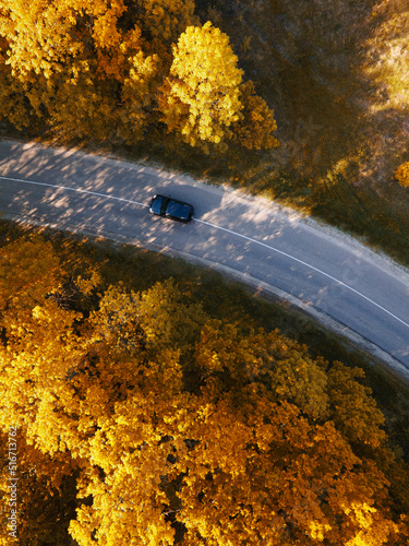 winding rual road inside autumn forest with black car photo