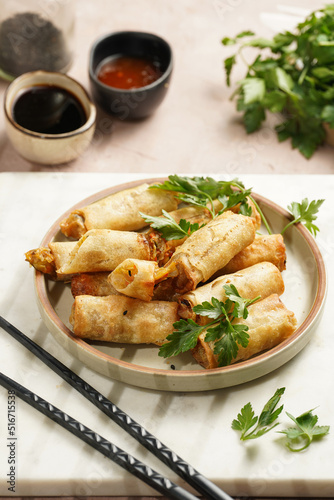 Traditional southeast asian starter dish spring or summer rolls - deep fried dim sum dumplings stuffed with vegetables with soy sauce, fresh coriander on grey plate with black chop sticks, top view