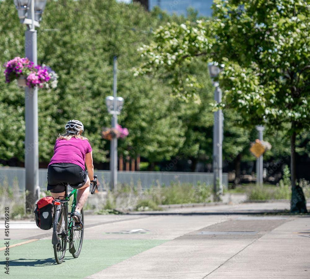 Fototapeta premium Woman in a colorful t-shirt practices cycling on a bike path in an urban city