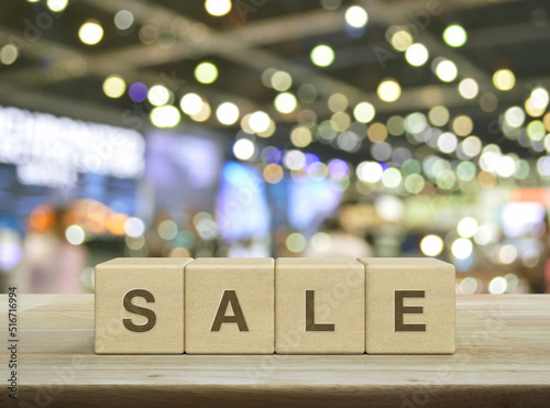 SALE letter on wood block cubes on wooden table over blur light and shadow of shopping mall, Business sales and discounts concept © grapestock