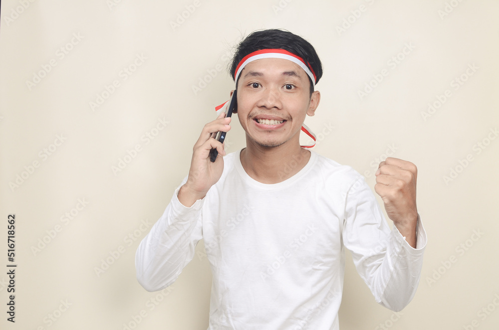 Indonesian man smiling while holding a mobile phone during independence day celebration Indonesian man smiling while holding a mobile phone during independence day celebration