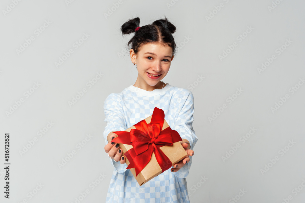 Happy pretty young dark-haired girl smiling and showing gift box at camera, standing in trendy t shirt over light grey background. Teenage girls in love, Receiving gifts from lovers Happy pretty young dark-haired girl smiling and showing gift box at camera, standing in trendy t shirt over light grey background. Teenage girls in love, Receiving gifts from lovers