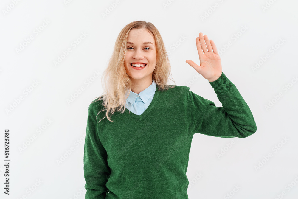Friendly cheerful blonde girl smiling, saying hi and waving hand to greet person, make hello gesture, welcome someone, wears casual clothes. Indoor studio shot on white background Friendly cheerful blonde girl smiling, saying hi and waving hand to greet person, make hello gesture, welcome someone, wears casual clothes. Indoor studio shot on white background