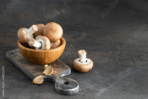 Uncooked Portobello mushrooms in wooden bowl on cut board ingredient background with copy space