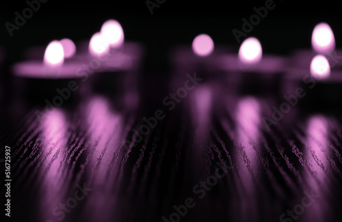 A group of tea candles blurred highlighted by strong purple lighting reflecting background.
