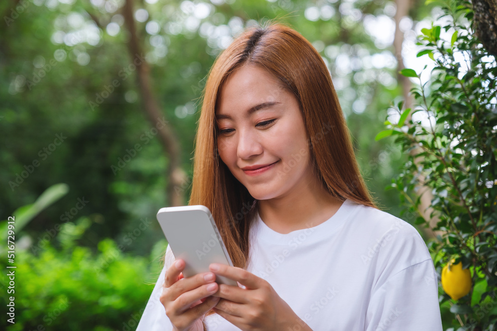 Portrait image of a beautiful young asian woman holding and using mobile phone in the outdoors