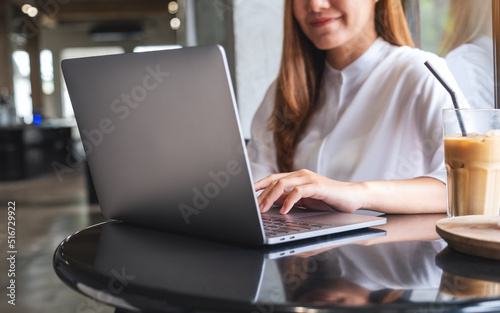 Closeup image of a woman working and typing on laptop computer keyboard with a glass of coffee on the table