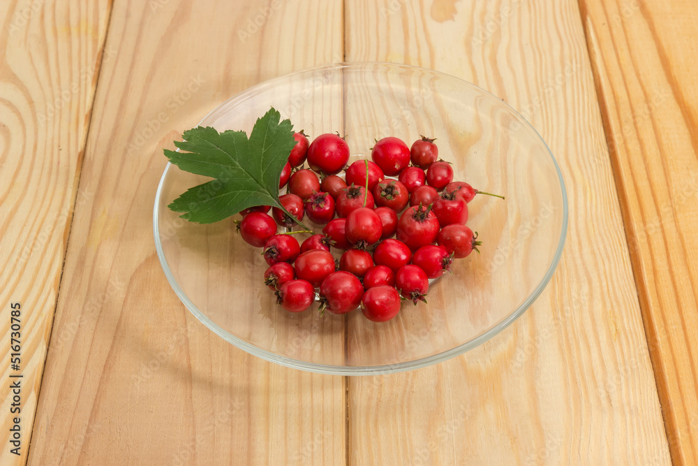 Hawthorn fruits on glass saucer with leaf on rustic table Hawthorn fruits on glass saucer with leaf on rustic table
