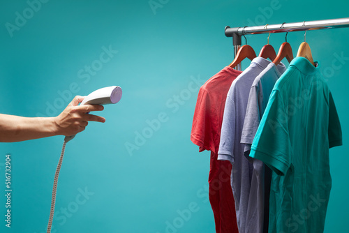 Males hand holds vertical steamer and using to iron colors t- shirts on blue background. photo