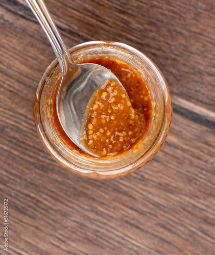 Top view of glass jar with bavarian mustard and spoon on wooden background.