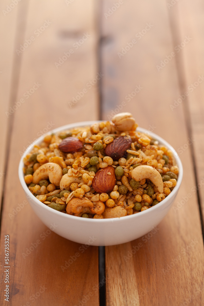 Close-up of Shahi Mixture made from almonds, cashew, corn flakes, peanut, Indian spicy snacks (Namkeen), in white ceramic bowl over wooden background Close-up of Shahi Mixture made from almonds, cashew, corn flakes, peanut, Indian spicy snacks (Namkeen), in white ceramic bowl over wooden background