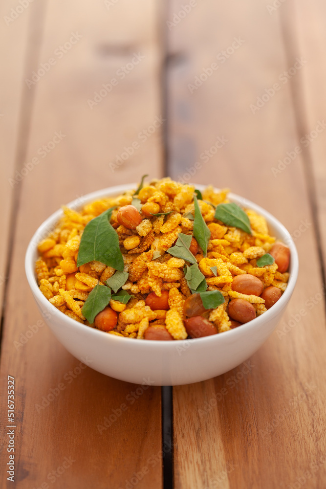 Close up of salted peanut mixed Indian namkeen (snacks) with green curry leaves in in white ceramic bowl over wooden background Close up of salted peanut mixed Indian namkeen (snacks) with green curry leaves in in white ceramic bowl over wooden background