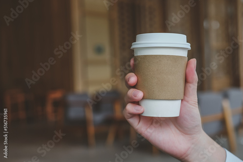 Man hand holding brown paper cup of hot coffee in coffee cafe. take away hot drink.