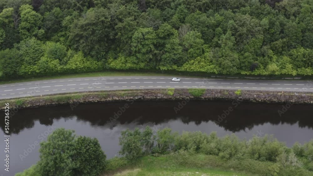 Single car drives on left side of road along forested country river Single car drives on left side of road along forested country river
