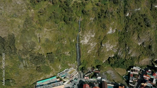 Cascada de la Virgen, Waterfall Flowing Down On Mossy Cliff To Baños de Agua Santa City In Ecuador. - aerial