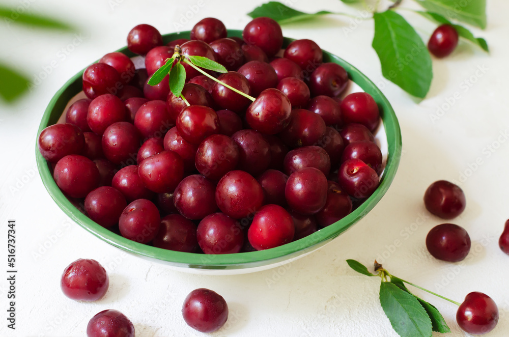 Many ripe red cherries in a white ceramic bowl with a green stripe on a light background. Harvesting concept. Horizontal orientation. Top view Many ripe red cherries in a white ceramic bowl with a green stripe on a light background. Harvesting concept. Horizontal orientation. Top view
