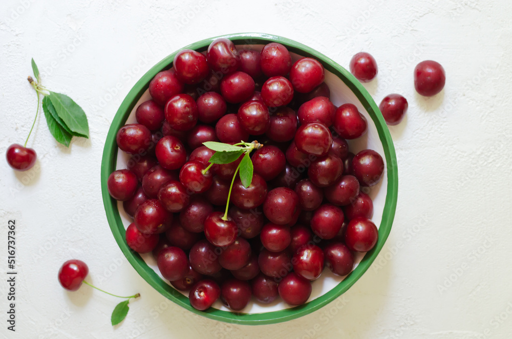Many ripe red cherries in a white ceramic bowl with a green stripe on a light background. Harvesting concept. Horizontal orientation. Top view Many ripe red cherries in a white ceramic bowl with a green stripe on a light background. Harvesting concept. Horizontal orientation. Top view