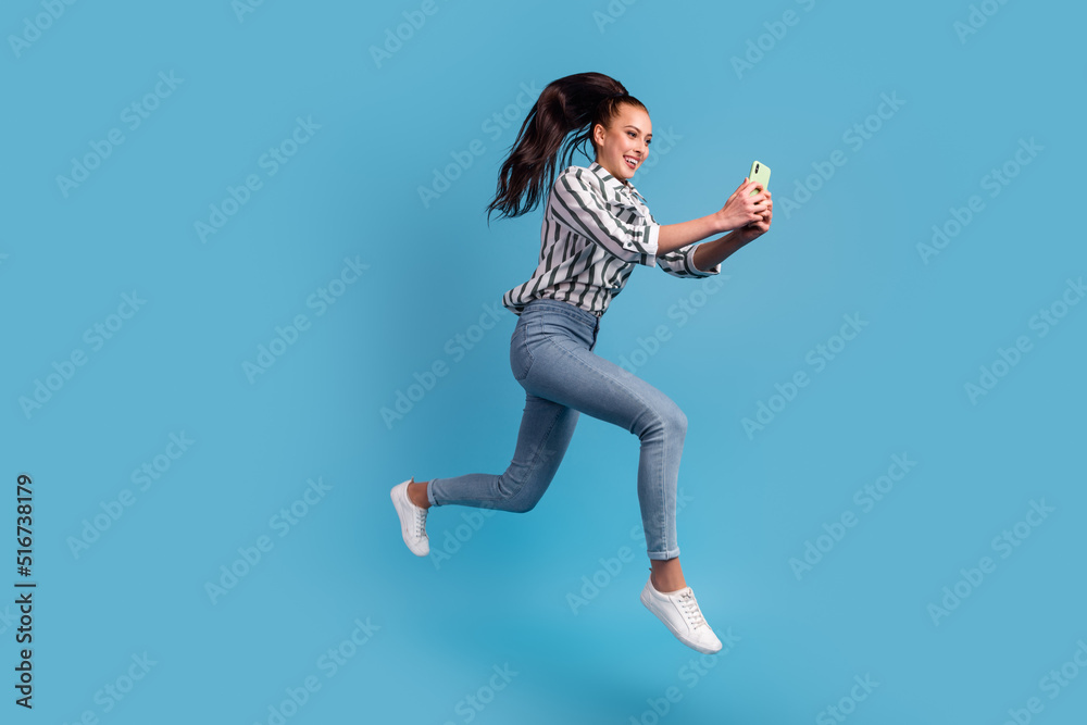 Photo of excited lady dressed shirt using 5g modern device jumping high smiling isolated blue color background
