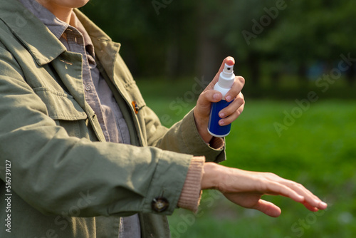 health care, protection and people concept - woman spraying insect repellent or bug spray to her hand at park photo