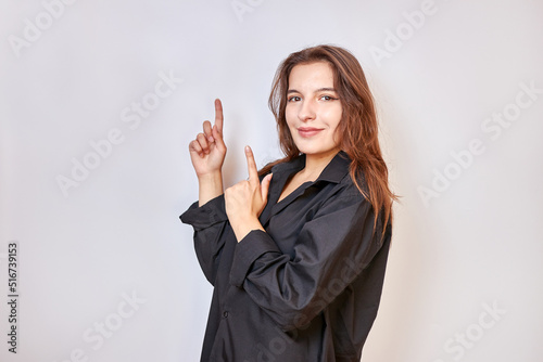 A beautiful girl in a black shirt shows a gesture pointing upwards with the fingers of both hands.