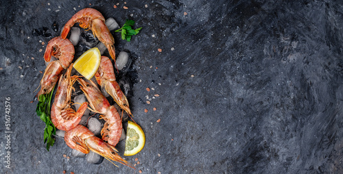 shrimps. wild ocean jumbo shrimps with ice and lemon, seafood shrimps prawns on ice frozen. Long banner format. top view