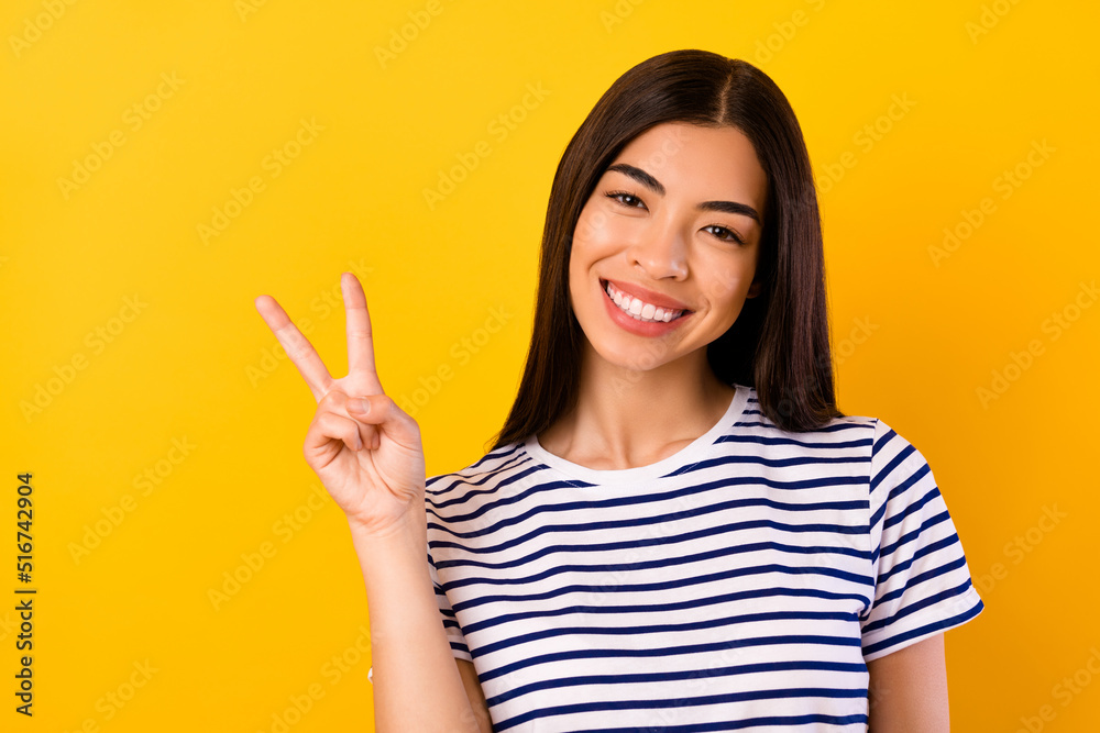 Photo of funny adorable girl dressed striped clothes showing v-sign smiling isolated yellow color background Photo of funny adorable girl dressed striped clothes showing v-sign smiling isolated yellow color background