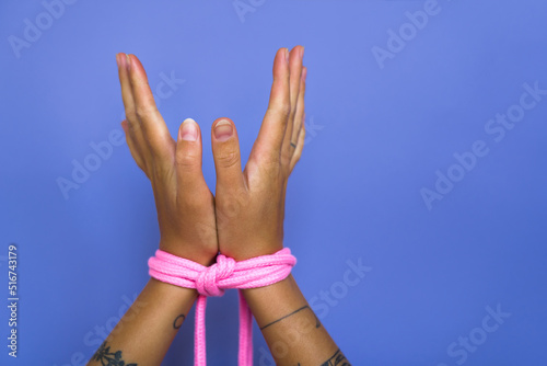 Cropped view of the tanned woman hands tied with bdsm bondage over violet studio wall