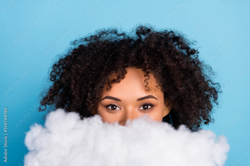 Portrait of attractive funny girly girl hhiding face behind white cloud isolated over bright blue color background Portrait of attractive funny girly girl hhiding face behind white cloud isolated over bright blue color background