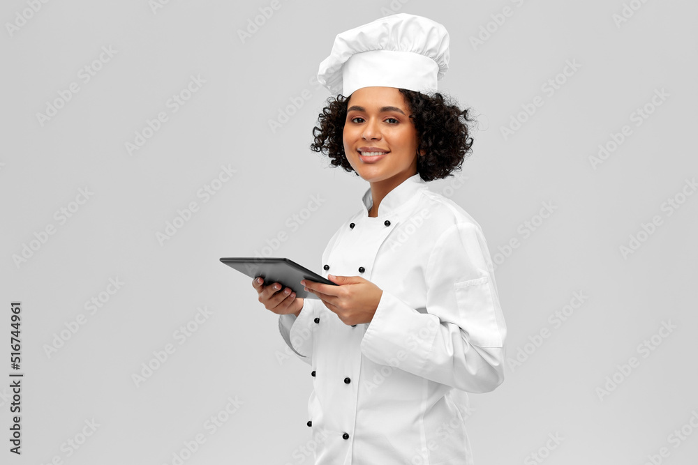 cooking, culinary and people concept - happy smiling female chef in toque and jacket with tablet pc computer over grey background cooking, culinary and people concept - happy smiling female chef in toque and jacket with tablet pc computer over grey background