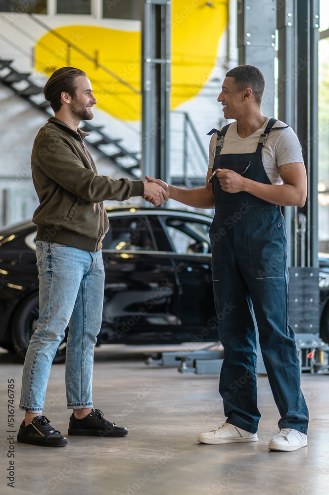 Cheerful car workshop worker shaking hands with the customer