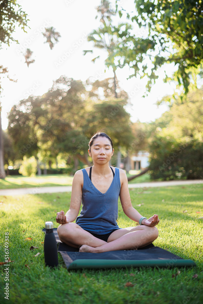 Asian young woman meditating outdoors on the grass in the park. She seems calmed. Asian young woman meditating outdoors on the grass in the park. She seems calmed.