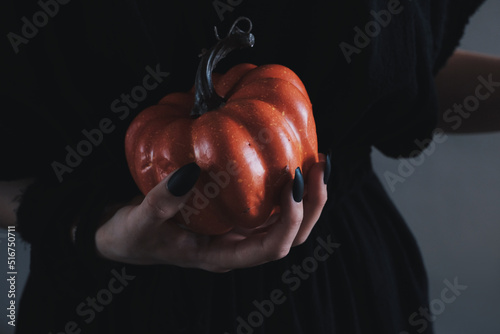 Close up halloween pumpkin in the witch's hand with long black nails. Halloween aesthetic. Black witch.